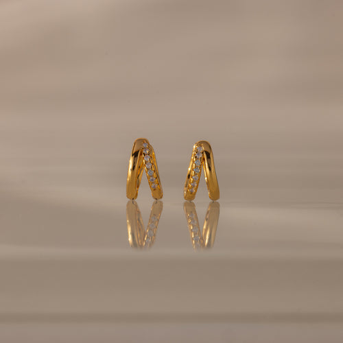 Amelia Duo Opal Huggies—gold hoop earrings with opal accents—are styled as modern huggies and displayed on a reflective beige surface.
