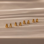 Eight pairs of earrings, including the Amelia Duo Onyx Huggies and modern intertwined hoops, are displayed on a beige surface with soft shadows.