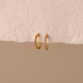The Inside Out Diamond Huggies, gold hoop earrings adorned with sparkling diamonds, are displayed against a textured beige surface.