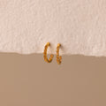 The Inside Out Topaz Huggies are small gold gemstone earrings with embedded stones, ideal for stacking, shown on a textured off-white surface.