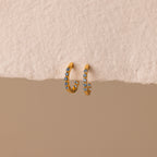 Inside Out Aquamarine Huggies: Gold hoop earrings featuring small blue aquamarine stones. Perfect for stacking or wearing solo, shown on a textured beige surface.
