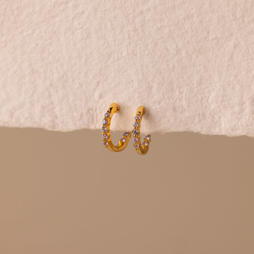 Inside Out Alexandrite Huggies featuring small gemstones, shown on a textured off-white surface with a beige background.