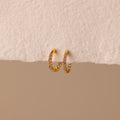 Inside Out Alexandrite Huggies featuring small gemstones, shown on a textured off-white surface with a beige background.