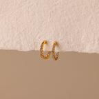 Inside Out Alexandrite Huggies featuring small gemstones, shown on a textured off-white surface with a beige background.