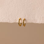 Inside Out Peridot Huggies are gold hoop stacking earrings featuring small green gemstones, perfect as birthstone huggie earrings. Shown on a textured off-white surface with a beige background.