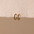 The Inside Out Sapphire Huggies feature gold hoops with small blue gemstone accents, perfect for stacking, shown on a textured off-white background.