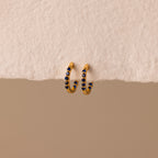 The Inside Out Sapphire Huggies feature gold hoops with small blue gemstone accents, perfect for stacking, shown on a textured off-white background.