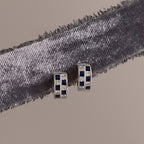 Royal Blue Checkered Huggies in Sterling Silver featuring royal blue and clear stones, displayed on a textured gray ribbon.