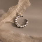The Pearl Moon Charm, a crescent-shaped pearl earring inspired by celestial beauty, is displayed on soft cream-colored fabric.