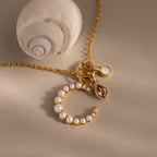 The Pearl Moon Charm in 18K Gold, adorned with delicate accents and shown beside a spiral seashell on a beige surface, is perfect for lovers of celestial-inspired jewelry.