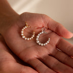 A hand displays two crescent-shaped pendants, one gold and one silver, adorned with pearls—elegant Pearl Moon Charm in White Gold necklaces that beautifully capture celestial allure.