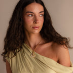Woman with long curly hair in a cream off-shoulder dress, looking to the side, wearing the Pearl Moon Charm in 18K Gold.