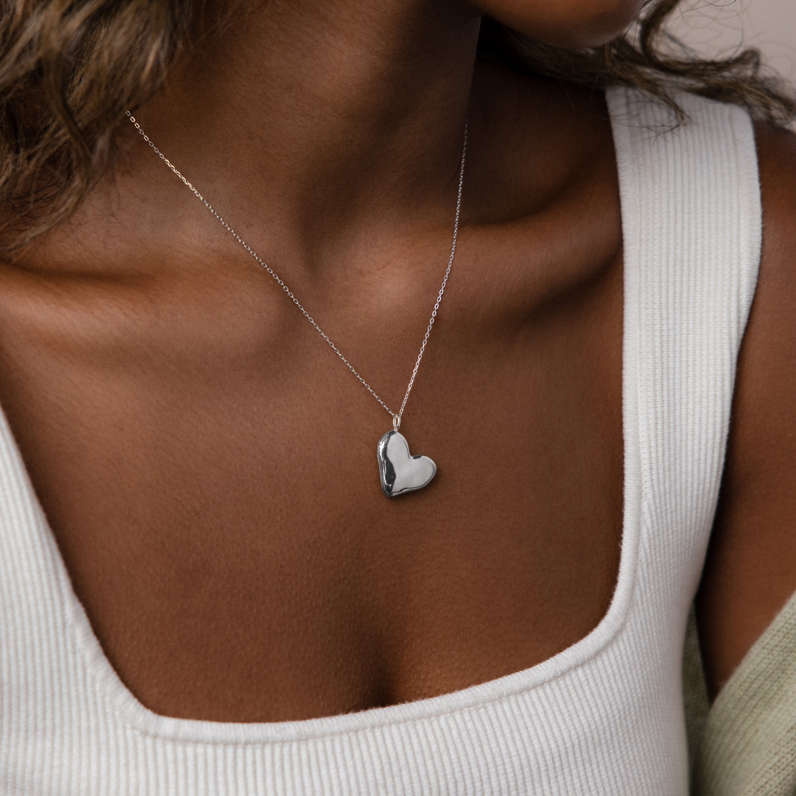 A woman wearing a white tank top and the Organic Heart Locket Necklace, featuring a delicate heart-shaped pendant.