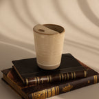 The Everyday Ceramic Mug in beige with a speckled glaze sits atop stacked vintage books, soft shadows behind.