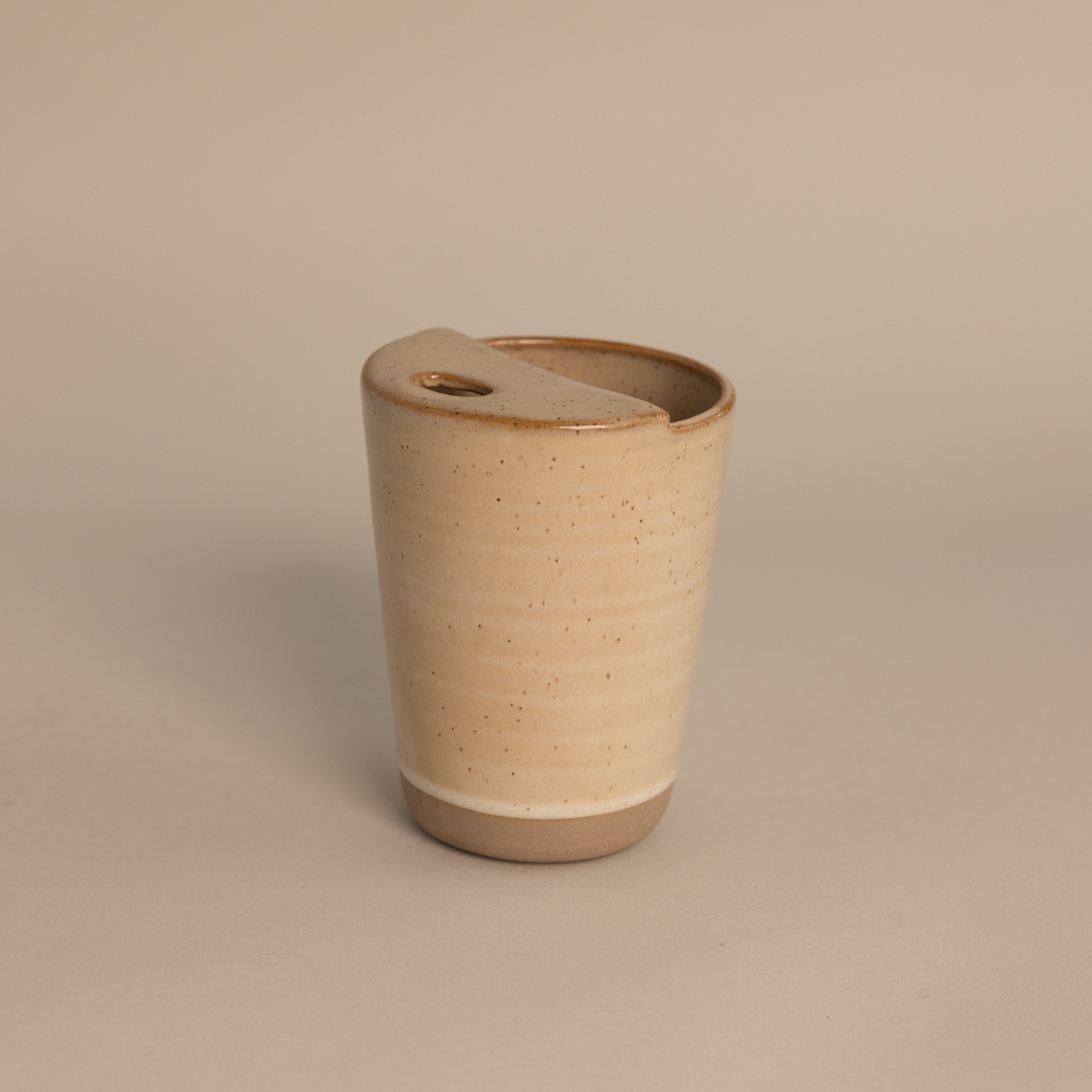 The Everyday Ceramic Mug comes with a matching lid and features a subtle speckled beige glaze, shown against a light neutral background.