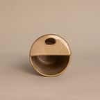 The Everyday Ceramic Mug is round and beige with a half-covered top, oval cutout handle, and subtle speckled glaze, shown on a neutral background.