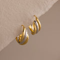 The Intertwined Mixed Metal Hoops are gold and silver twisted hoop earrings, displayed on a textured off-white surface.