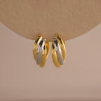 The Intertwined Mixed Metal Hoops feature gold and silver twisted hoops, creating a striking two-tone look against a neutral backdrop.