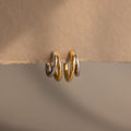 Two pairs of Mixed Metal Duo Hoops—featuring gold and silver—rest elegantly on beige paper, highlighting their modern hoop earring design.