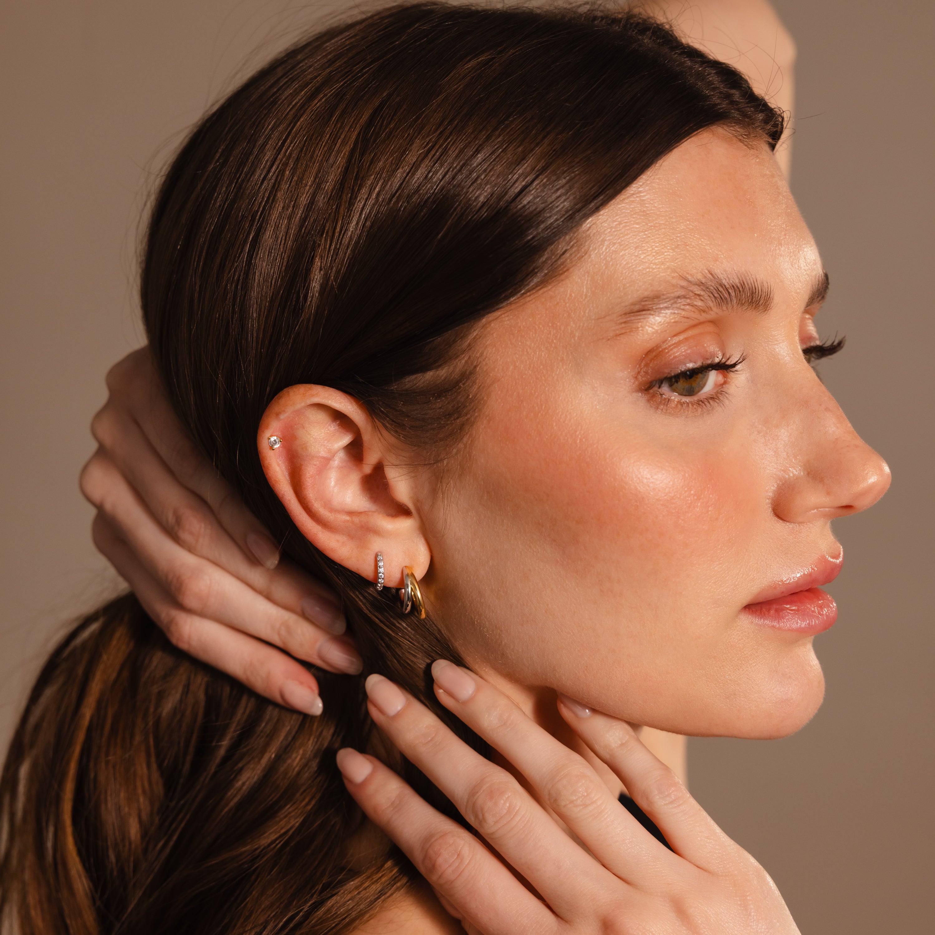 Woman with brown hair and glowing skin models the Mixed Metal Duo Hoops, displaying her manicured nails as she gazes to the side.