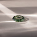 The Skinny Agate Ring, featuring green marbling, is displayed on a smooth, light surface with subtle shadows—an ideal accessory for gemstone enthusiasts.