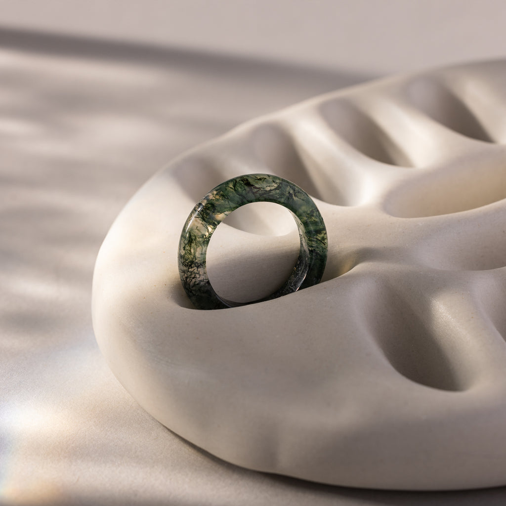 The Skinny Agate Ring, featuring unique green marbling, sits on a beige wavy ceramic dish in gentle natural light—a must-have accessory for gemstone lovers.