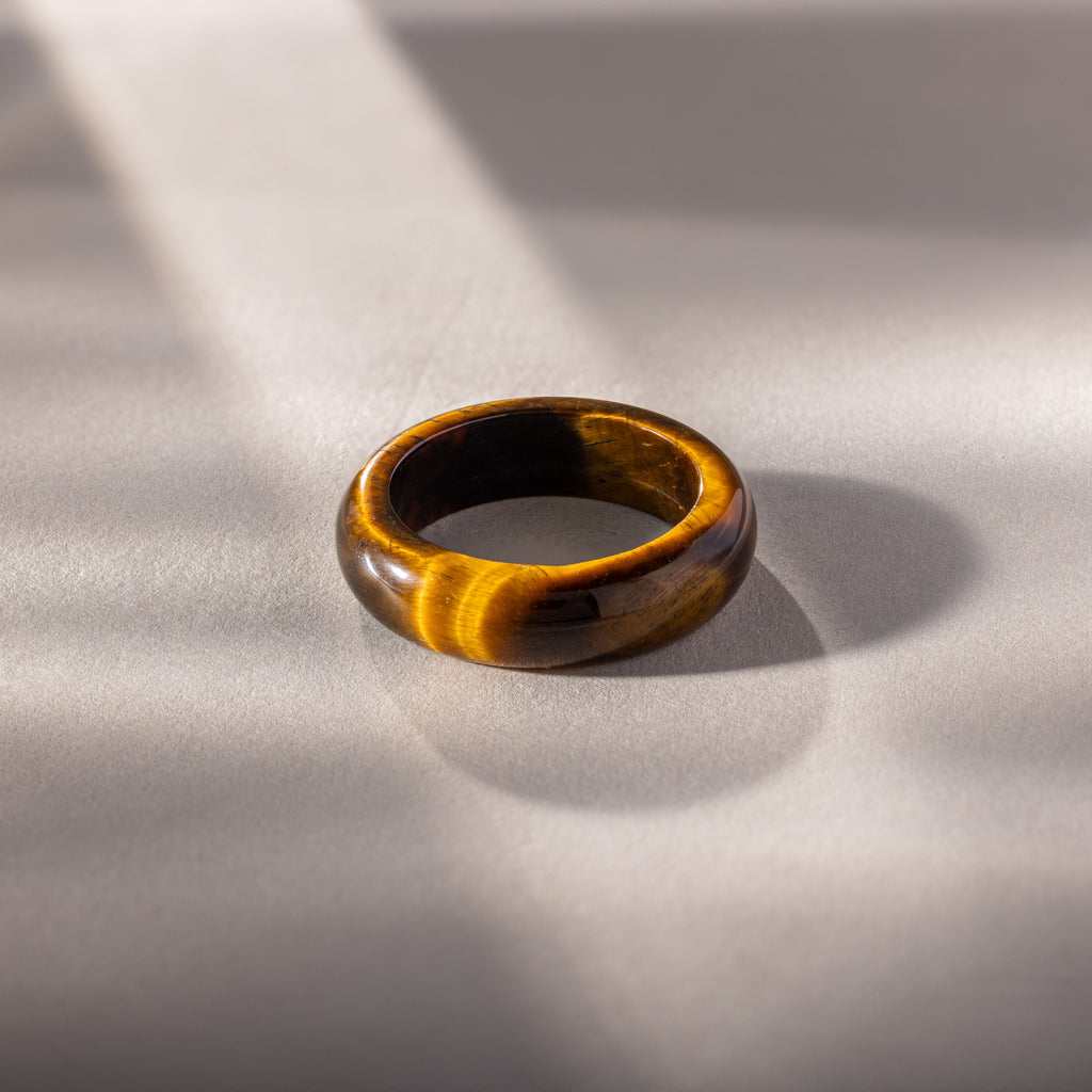Experience earthy elegance with the Skinny Tiger's Eye Ring, featuring a rich brown gemstone set on a light gray surface in soft sunlight. Ideal as a stacking ring for a refined, natural look.