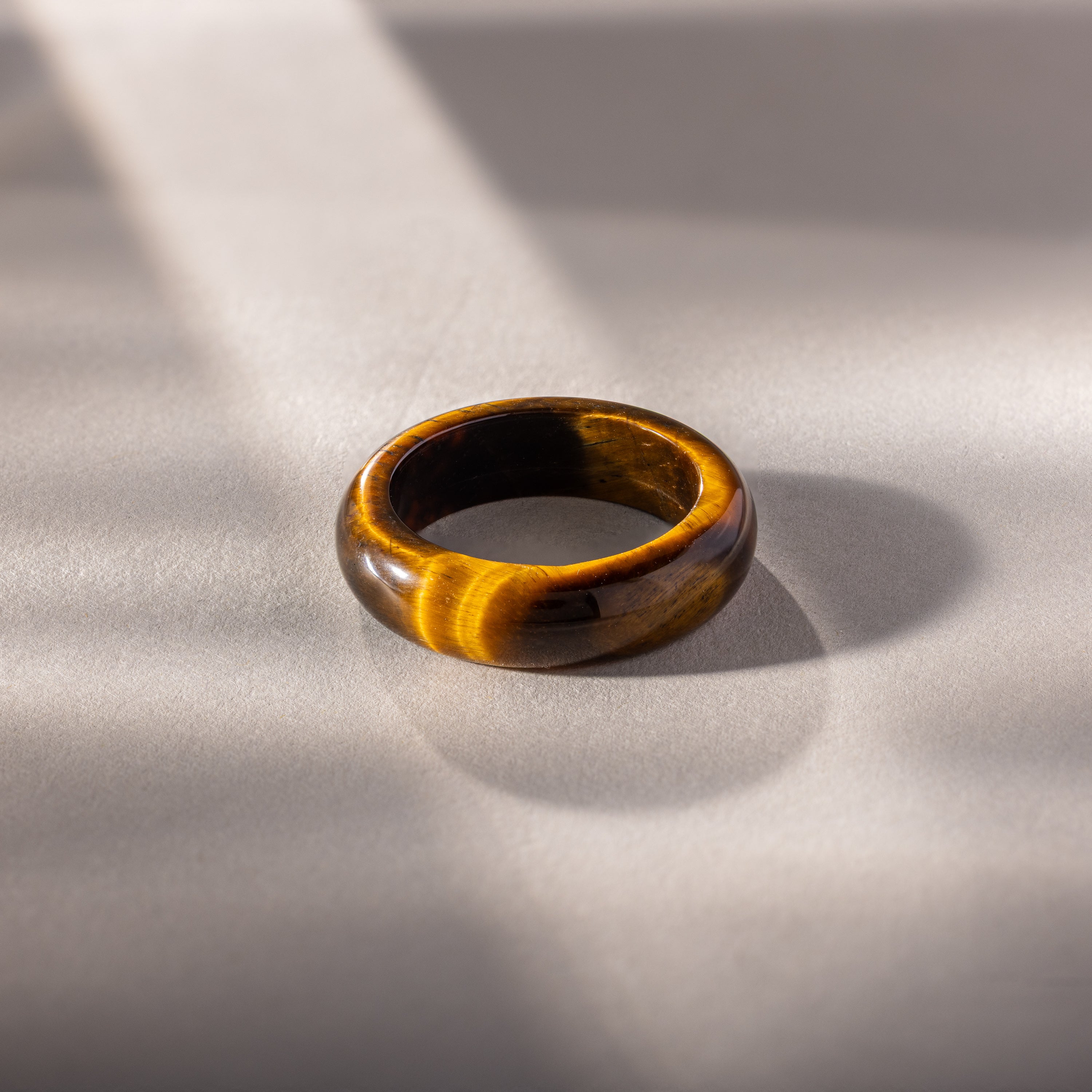 Experience earthy elegance with the Skinny Tiger's Eye Ring, featuring a rich brown gemstone set on a light gray surface in soft sunlight. Ideal as a stacking ring for a refined, natural look.