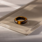The Skinny Tiger's Eye Ring, ideal for stacking, is displayed on a clear acrylic block and illuminated by natural light—an elegant, earthy accessory.