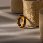 The Skinny Tiger's Eye Ring stands upright against textured beige ceramic shapes on a softly lit surface, showcasing the natural allure of earthy jewelry.