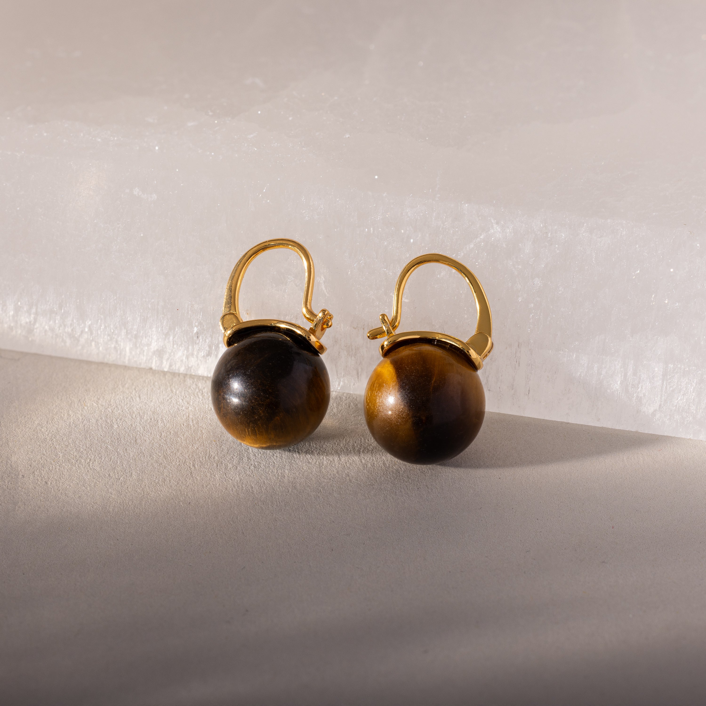 Tiger's Eye Dome Drop Earrings in 18K Gold feature round, polished beads on gold leverbacks, displayed on a light textured surface—a timeless piece of natural stone jewelry.