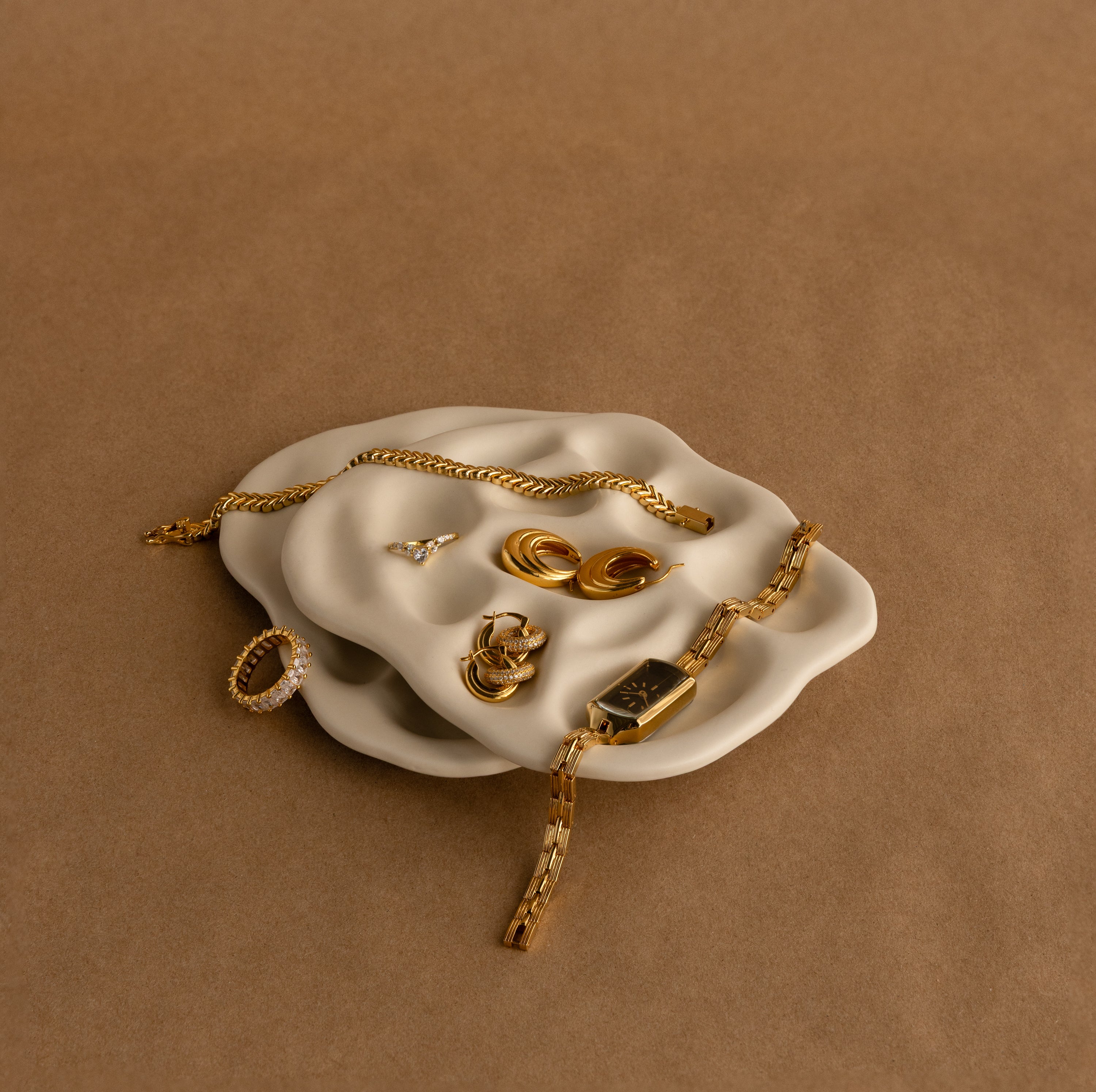 Gold rings, bracelets, earrings, and a watch elegantly displayed on the Mini Organic Treasure Trove Jewelry Dish, serving as a stylish keepsake holder.