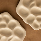The Mini Organic Treasure Trove Jewelry Dish features two wavy, cream-colored ceramic dishes with unique shapes, ideal for holding keepsakes or jewelry on any surface.