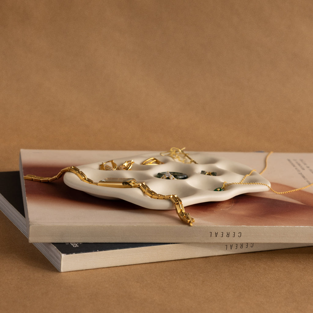 The Mini Organic Treasure Trove Jewelry Dish, crafted from white ceramic with gold jewelry, sits atop two books against a brown background—perfect as a mini jewelry dish or keepsake holder for your cherished items.