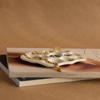 The Mini Organic Treasure Trove Jewelry Dish, crafted from white ceramic with gold jewelry, sits atop two books against a brown background—perfect as a mini jewelry dish or keepsake holder for your cherished items.