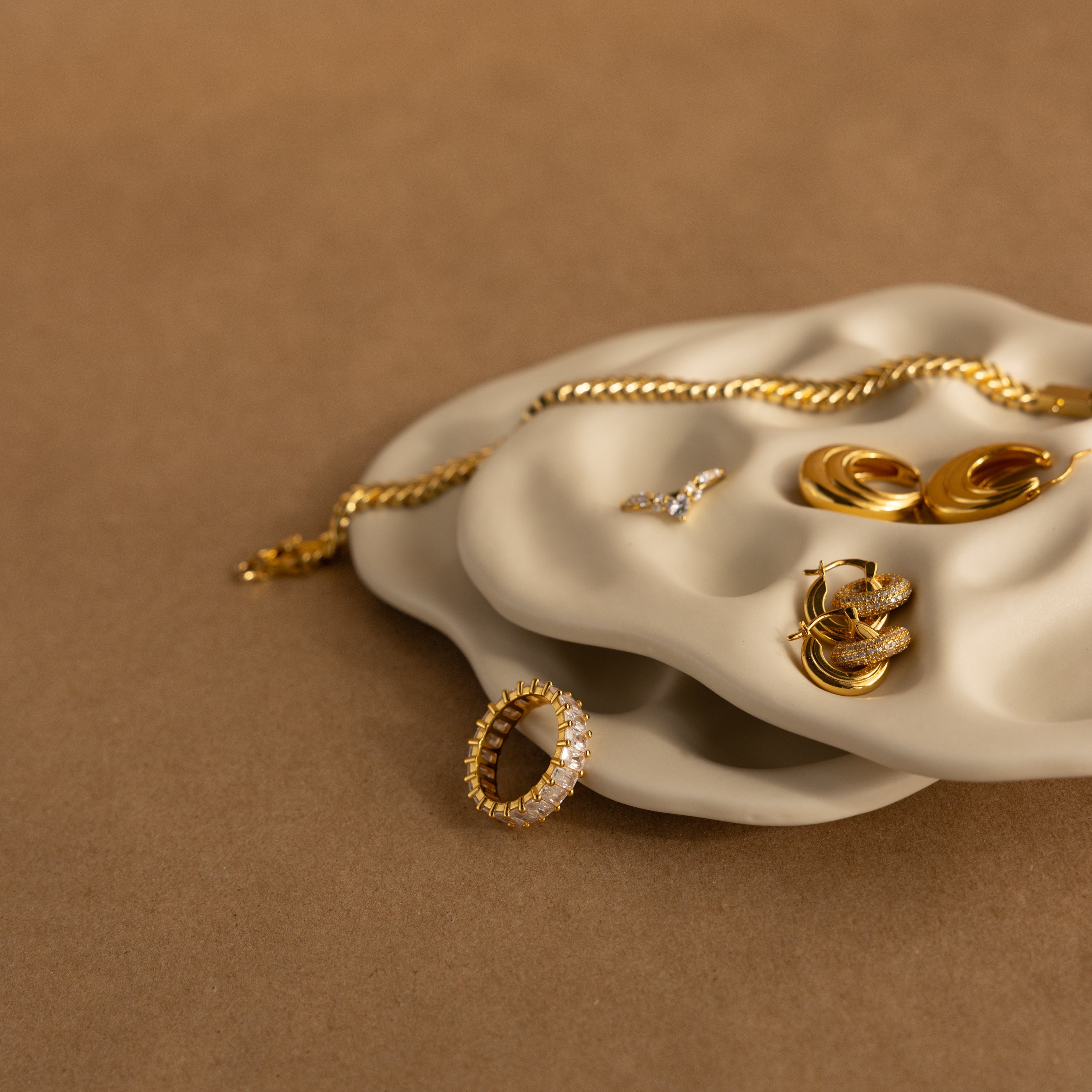 Gold rings, earrings, and a bracelet rest on the Mini Organic Treasure Trove Jewelry Dish, which also serves as a keepsake holder, set against a brown background.