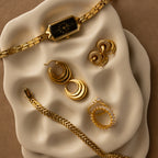 Gold jewelry and a watch, including earrings and bracelets, are displayed on the wavy cream Mini Organic Treasure Trove Jewelry Dish.