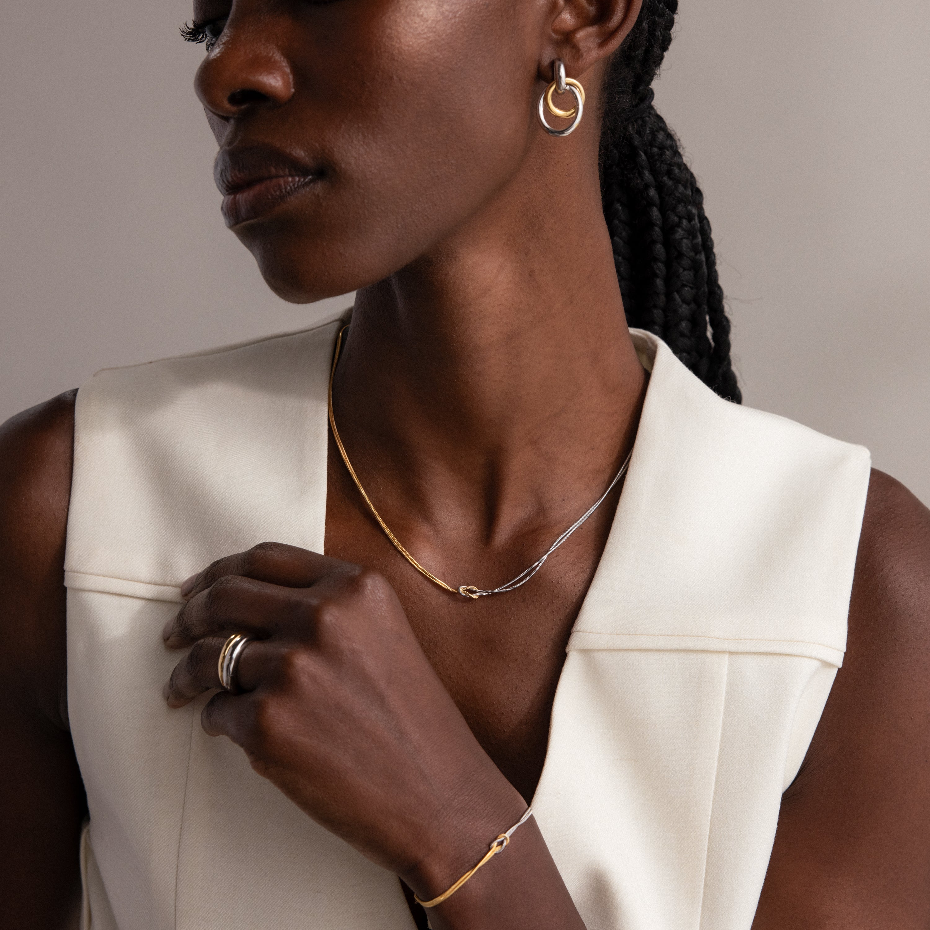 A woman poses with her hand near her collarbone, wearing a gold and silver Love Knot Chain Necklace over a white sleeveless top.