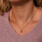 A woman wears the Gemstone Bubble Initial Necklace featuring a gold J pendant over a light purple fuzzy sweater.