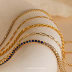 Five Mystery Jewelry gold necklaces, each with a distinct chain style—including one accented with blue gemstones—are elegantly displayed on a curved surface, offering whimsical charm for fans of unique accessories.