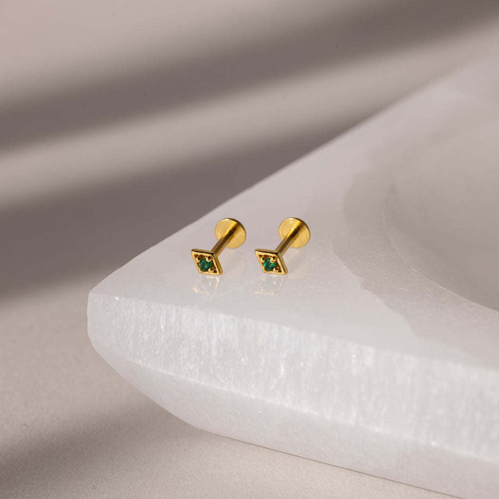 Gold geometric flat back emerald studs on a white surface