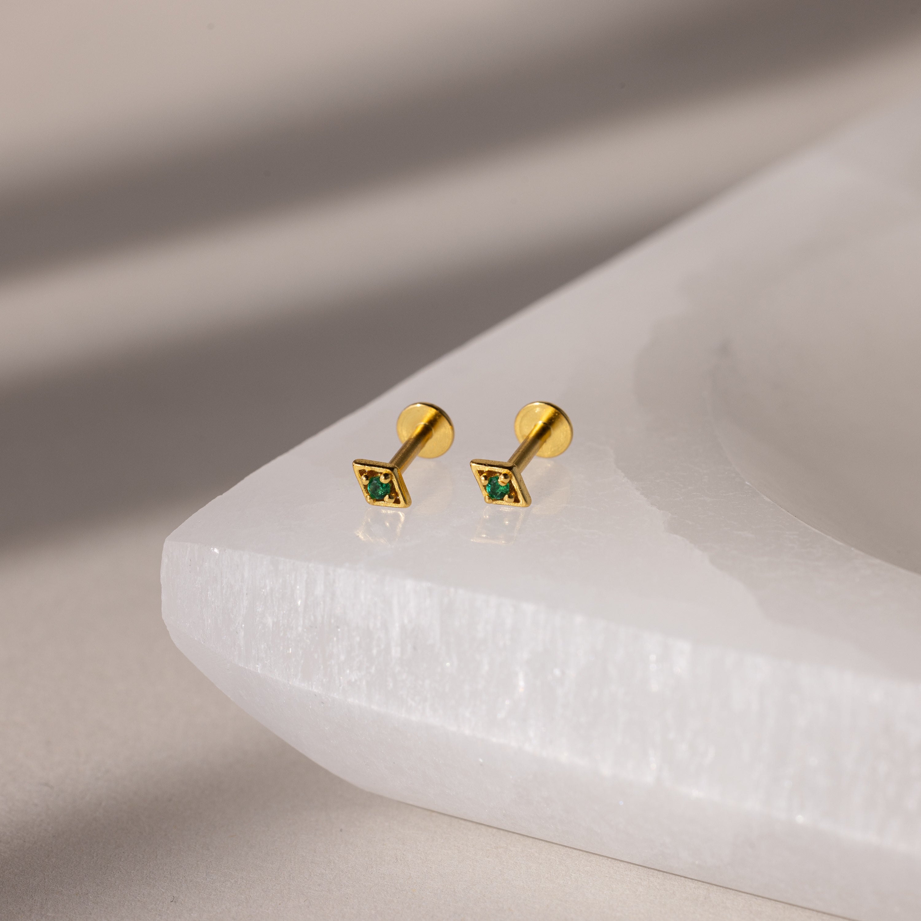Gold geometric flat back emerald studs on a white surface