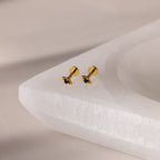 Gold geometric flat back sapphire stud earrings on a white stone surface