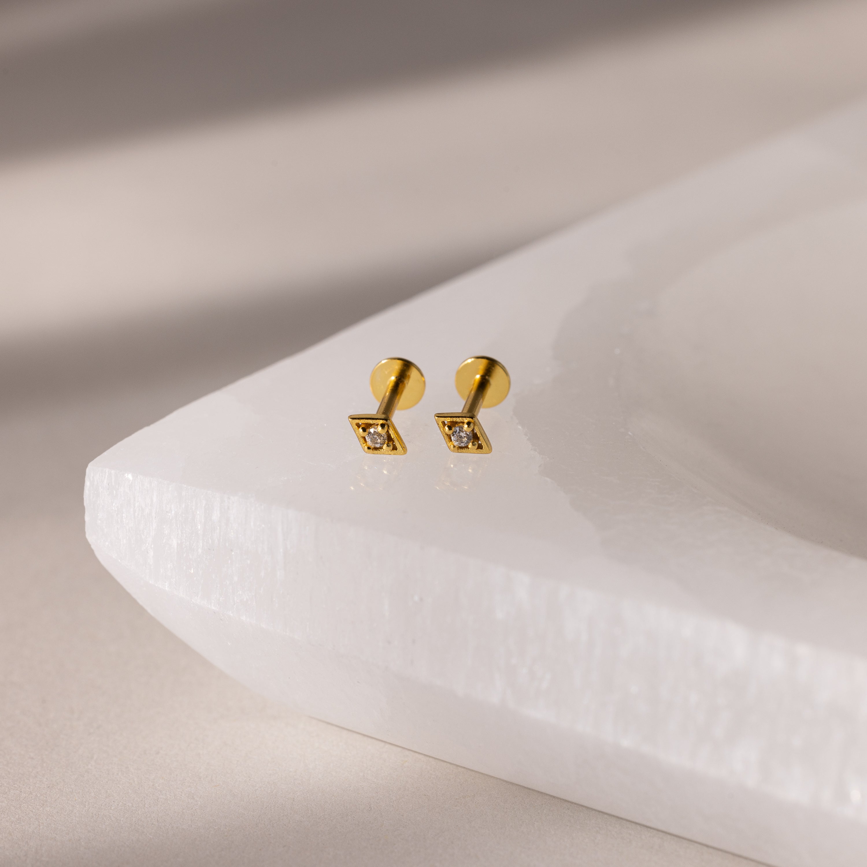 Gold geometric flat back diamond stud earrings on a white surface