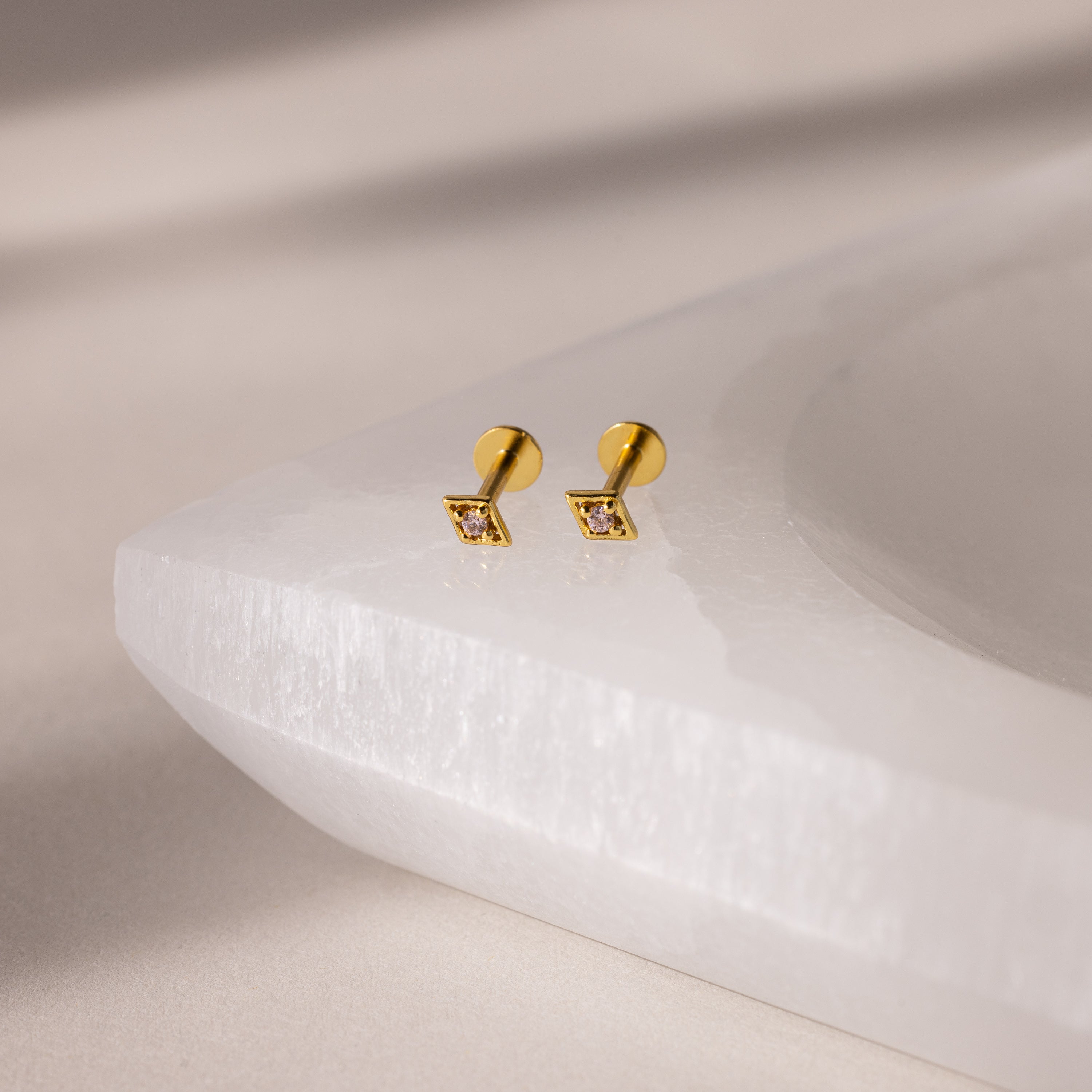 Geometric Pink Tourmaline Flat Back Studs—gold square earrings with clear stones inspired by geometric designs, shown on a white textured jewelry tray.