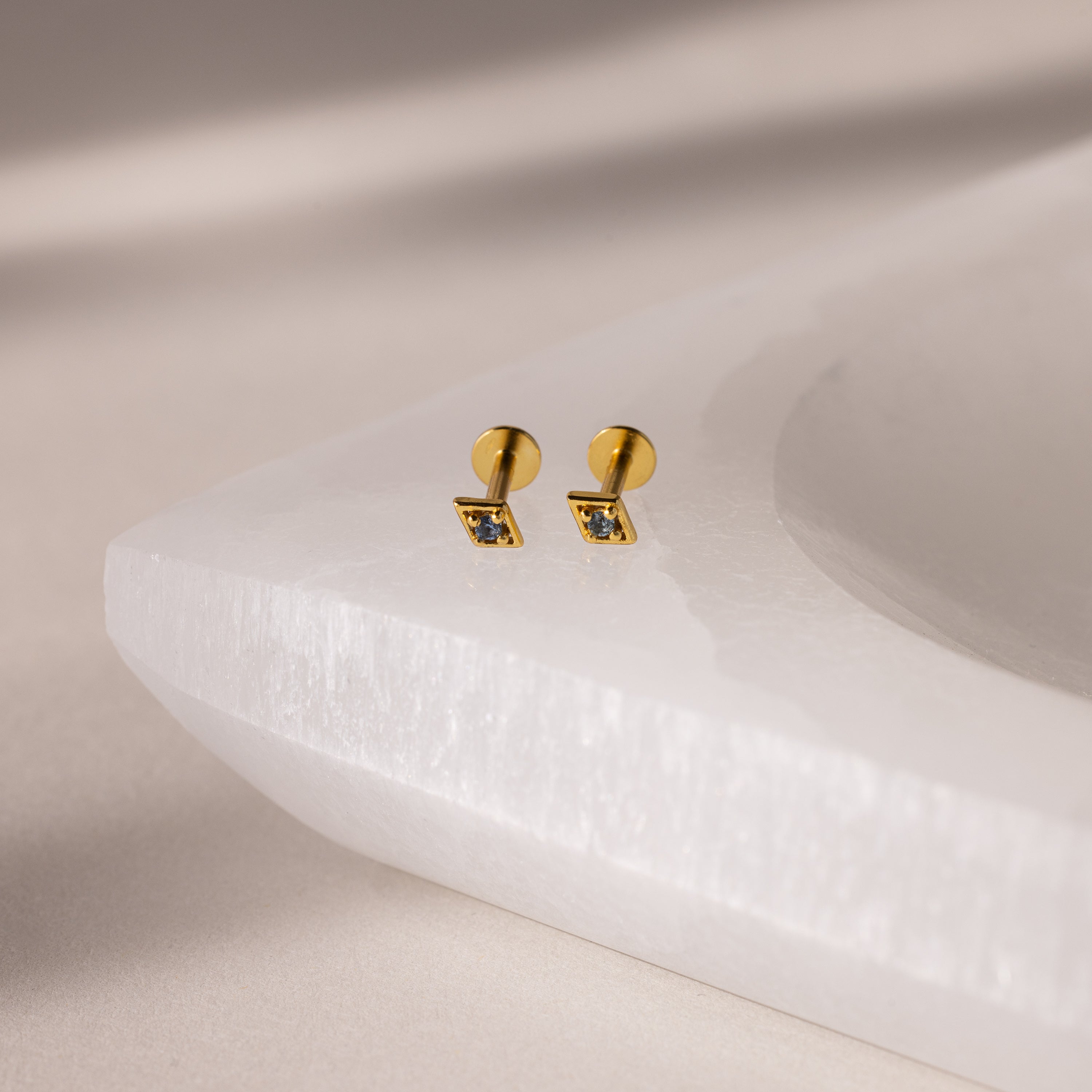 Gold geometric flat back aquamarine stud earrings on a textured white surface