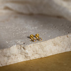 Gold geometric flat back alexandrite stud earrings on a textured stone surface