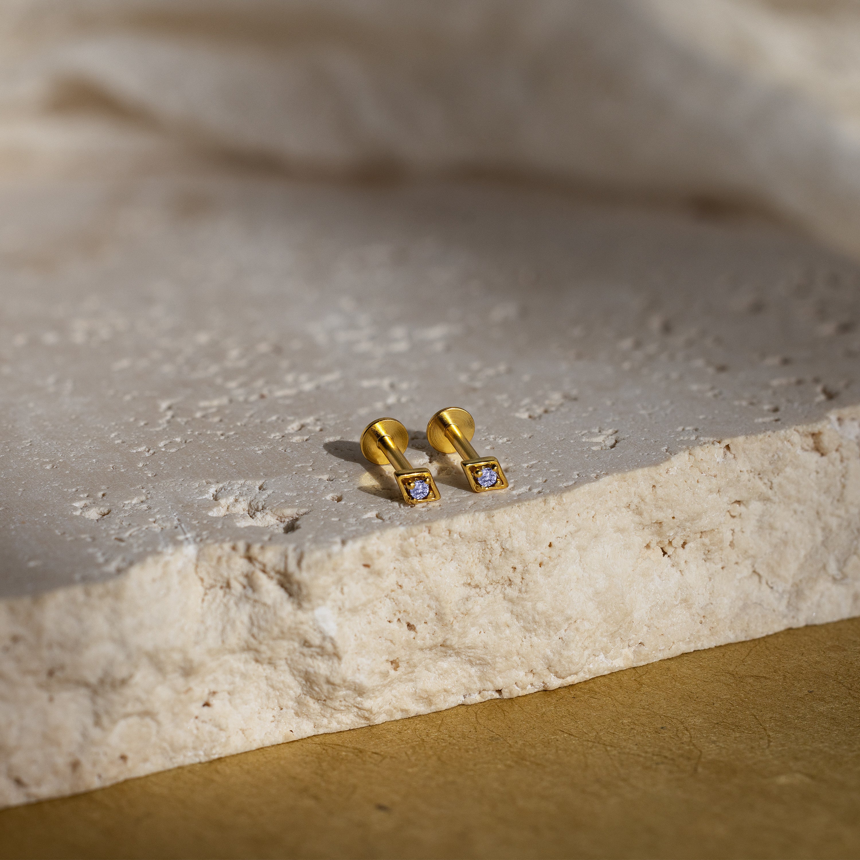 Gold geometric flat back alexandrite stud earrings on a textured stone surface