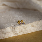Gold geometric flat back amethyst stud earrings on textured stone surface with soft natural lighting