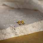 Gold geometric flat back blue topaz stud earrings on a textured stone surface